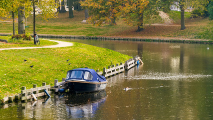 A boat on the city lake, autumn, along with cars parked on the street, white residential buildings and green grass.