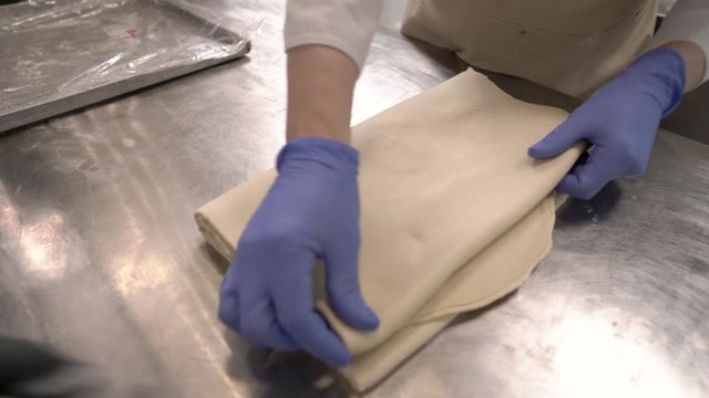 A close-up demonstration video of an expert chef squaring laminated dough, and placing it on a baking tray. Making croissant and bakery products
