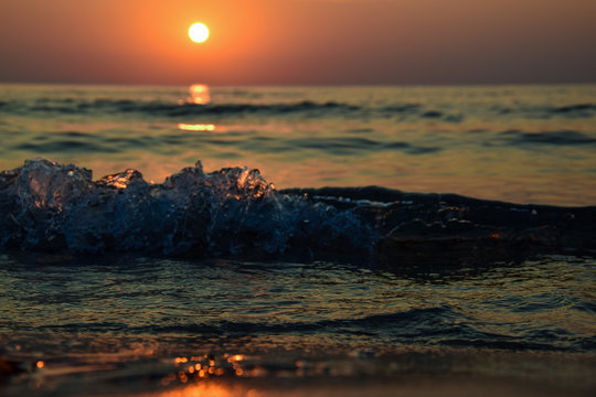 sunrise at the shore of the sea and ocean, seen from the sand level, with the glowing wave of water, and pleasant bokeh