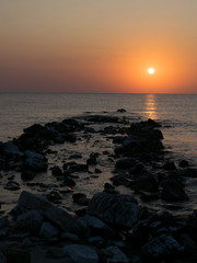sunrise at the seashore, among the rocks coming out of the water, with orange sun