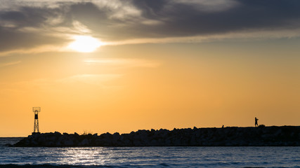 male silhouette on rocks, at sunrise, at sea or ocean shore