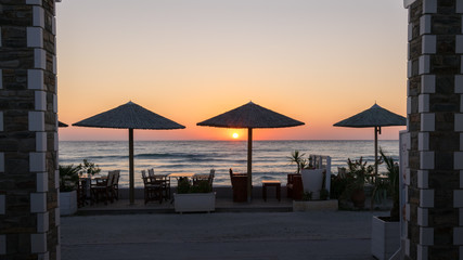 sunrise on the seafront with reed sun silhouette umbrellas, the sea with waves and dinner table.