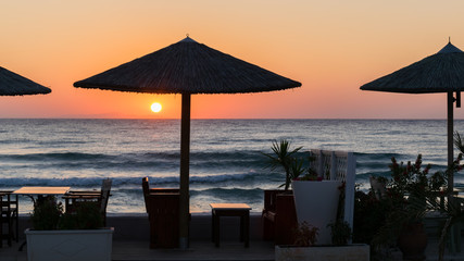 Fototapeta premium sunrise on the seafront with reed sun silhouette umbrellas, the sea with waves and dinner table.