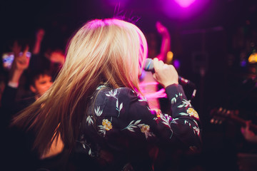 Beauty model girl singer with a microphone singing and dancing over holiday glowing background....