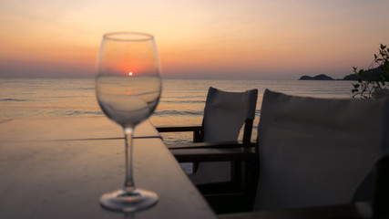 the sunrise seen through a glass on the table, with chairs and calm sea water.