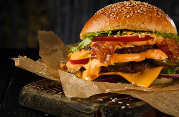 Cheeseburger with Two Beef Patties, Cheddar Cheese, Bacon, Iceberg Lettuce, Sliced Tomatoes and Red Onion on Cutting Board.