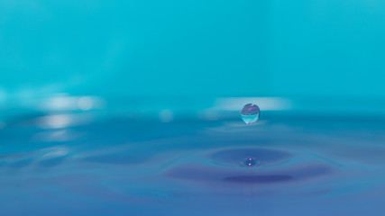 water splash in colorful background with a drop of water flying from above