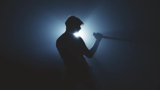 Man singer in the smoke and light sings into a microphone and dance. Dark background. Silhouette