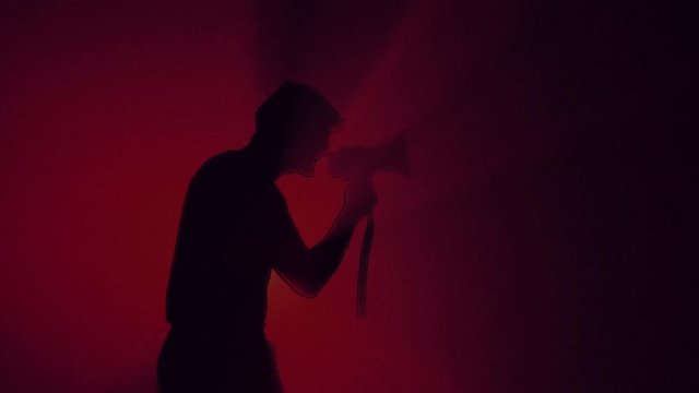 Angry Man Yells into the Loudspeaker. Dark Red background. Silhouette with black cartoon outlines. Protester. Riot concept.