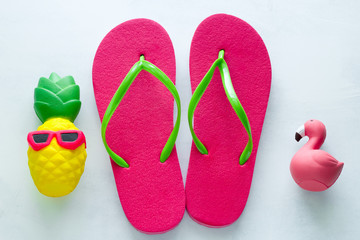 pink beach flip flops  and squishy toy pineapple in sunglasses and flamingo  on white  background copy space