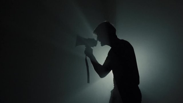Angry Man Yells into the Loudspeaker. Dark background. Silhouette. Protester.