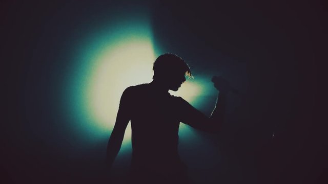 Man singer in the smoke and light sings into a microphone and dance. Dark background. Contrasting Silhouette