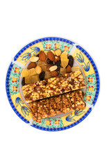 vegan dessert: several cereal bars with raisins and honey are on a bright plate, a lot of nuts and candied fruits are lying around, short focus
