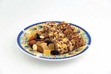 vegan dessert: several cereal bars with raisins and honey are on a bright plate, a lot of nuts and candied fruits are lying around, short focus