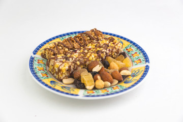 vegan dessert: several cereal bars with raisins and honey are on a bright plate, a lot of nuts and candied fruits are lying around, short focus