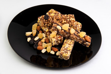 vegan diet: several cereal bars with nuts, raisins and honey, in a black plate on white, short focus