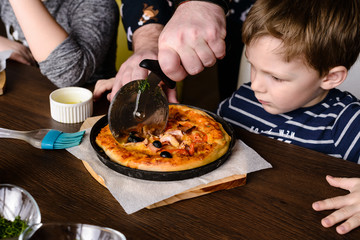 father cuts homemade pizza for a child into pieces
