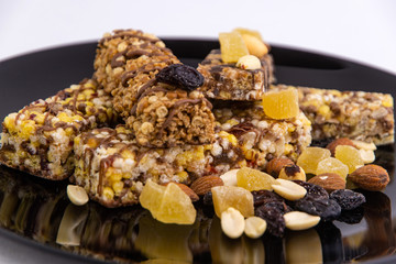 vegan diet: several cereal bars with nuts, raisins and honey, in a black plate on white, short focus