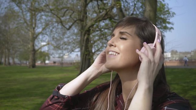 Caucasian female listening to music through headphones in slow motion in a park