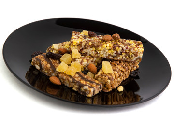 vegan diet: several cereal bars with nuts, raisins and honey, in a black plate on white, short focus