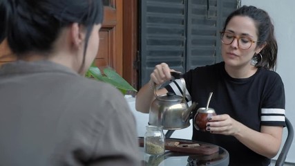 Two beautiful young woman talking and sharing a Mate, local beverage of Argentina and Uruguay at daytime
