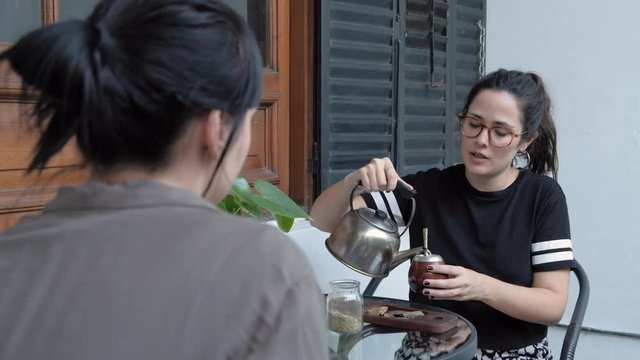 Beautiful young woman smiling, chatting with her friend and sharing a Mate, a local beverage of Argentina and Uruguay.