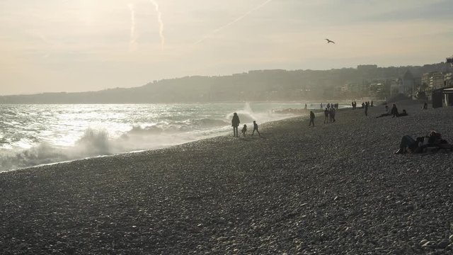 Families, people and tourists in silhouette playing on the shore and enjoying a sunny beach day in Nice, France.