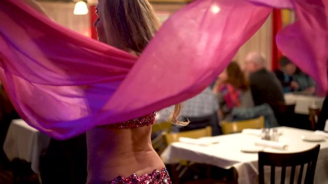 Slow motion closeup of belly dancer spinning with pink veil in a restaurant.