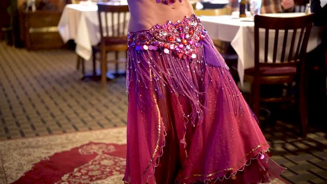 Slow motion of belly dancer’s skirts as she does body undulations in a restaurant.