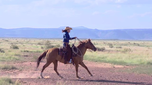 Side profile of Cowgirl Rancher riding horseback through wide open plains