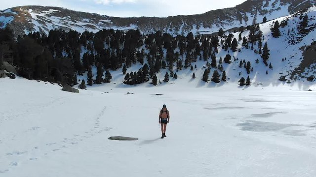 Man training cold endurance mediation, walking across beautiful frozen lake Pyrenees landscape without shirt or pants
