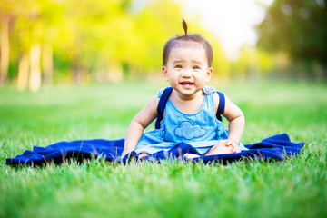 Naklejka na ściany i meble Happy baby sitting on the grass field laughing happily