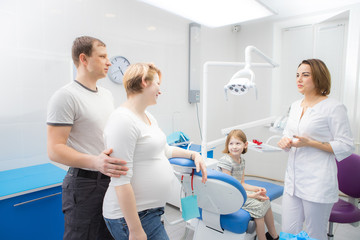 Fototapeta premium A female dentist communicates with a child and her family in a dental clinic. The mother of the girl is pregnant