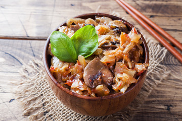 Stewed cabbage with mushrooms on the old wooden background in rustic style