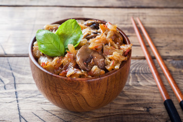Stewed cabbage with mushrooms on the old wooden background in rustic style