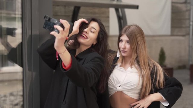 Two charming young girls are making a selfie on a professional camera. They are posing and making a differnt facial expression.