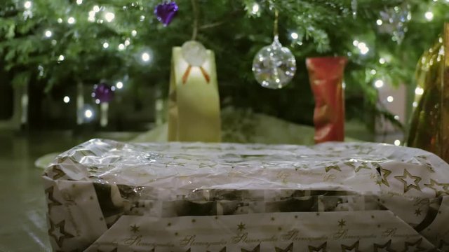 Male hands put a present under the Christmas tree. The Gift lies beneath the Pine which is nicely illuminated by a light string.
