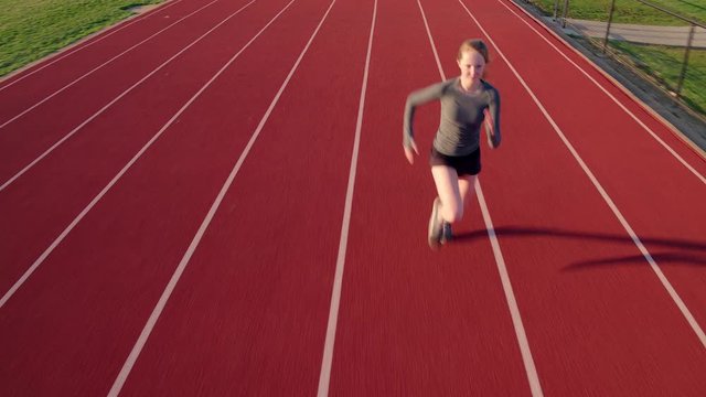 Teen girl athlete sprints on a high school track aerial camera preceding