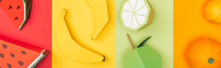 panoramic shot of origami watermelons, bananas, tangerines and lime on colorful striped paper