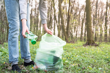 Cleaning-up the forest of plastic garbage. Person picks up a plastic bottle in the woods, concept of plastic awareness activism.