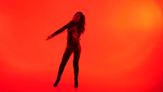 slim sensual young Asian girl in tight black leather clothes expressively plays the electric violin on a red background