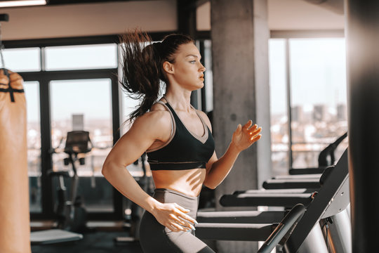 Young Sporty Muscular Brunette With Ponytail Running On Treadmill. Side View. I Can And I Will, Just Watch Me.