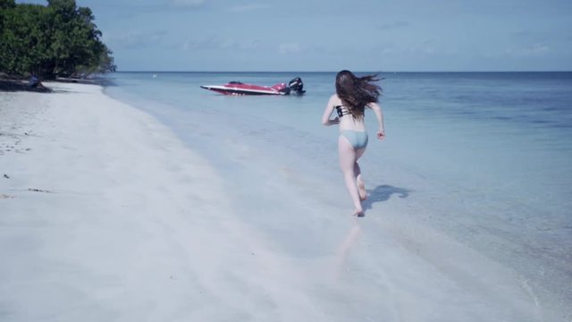SLOW MOTION: girl runs through the water to reach a bright red speed boat.