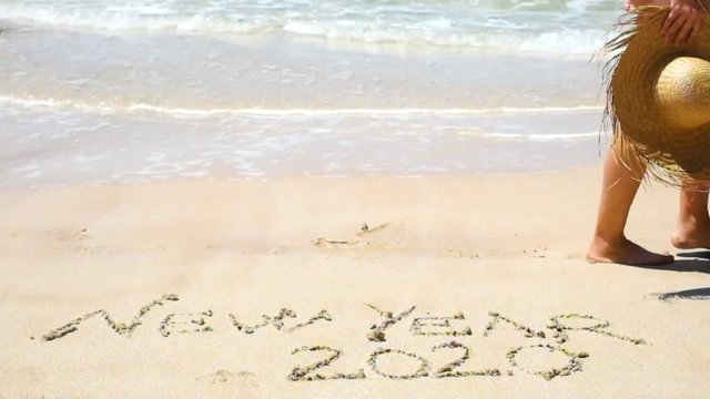 NEW YEAR 2020 EVE CONCEPT WITH TOURIST WOMAN WALKING ON THE SHORE AT THE BEAcH WITH THE WORDS WRITTEN ON THE SAND - People celebrating next year in tropical place for winter holiday