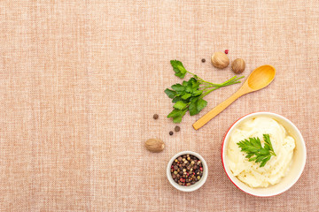 Warm mashed potatoes in a ceramic bowl with fresh parsley and dry spices. On a linen cloth background, copy space, top view