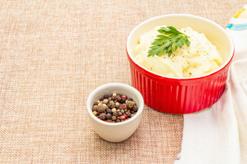 Warm mashed potatoes in a ceramic bowl with fresh parsley and dry pepper mix. On a linen cloth background, copy space, close up.