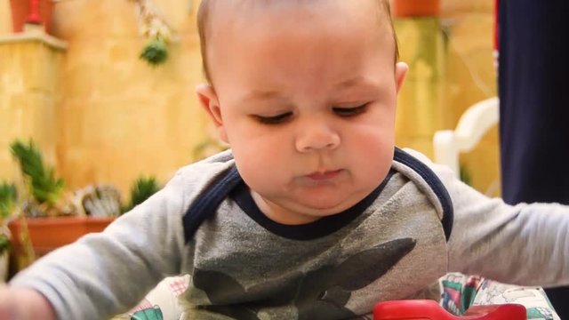 CLOSE UP of cute baby playing with the toy telephone on his walker then looks at camera