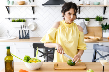 Young pretty woman cuts an avocado on a wooden salad board. Cooking. Preparation of fresh vegetable salad
