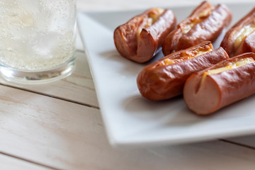 Roasted sausage with yellow cheese and a glass of soda over white wooden background