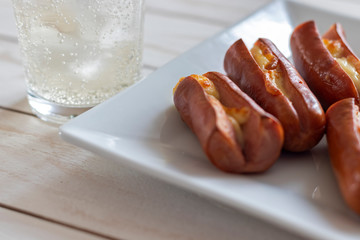 Roasted sausage with yellow cheese and a glass of soda over white wooden background
